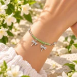 Pulsera Libélula Plata 925 en la muñeca de una mujer, con cristales verdes facetados y dos dijes de libélulas entre flores blancas.