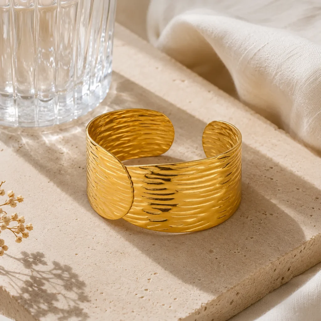 Brazalete dorado texturizado para mujer enchapado en Oro 18K con recubrimiento PVD sobre plataforma de piedra en fotografía lifestyle de Glow Secret.