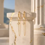 Aros Dorados Colgantes Gold Essential | Glow Secret Aros Dorados Colgantes Gold Essential de Glow Secret sobre pedestal inspirado en la arquitectura griega.