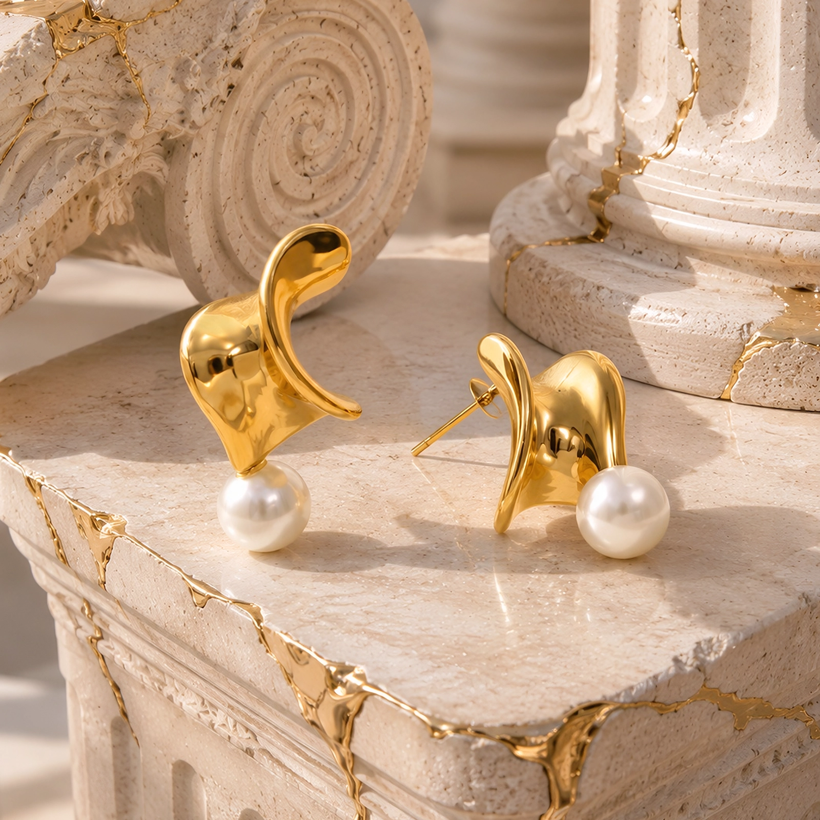 Aros Dorados con Perla de Glow Secret, con diseño geométrico irregular, acabado dorado y perlas blancas, sobre una superficie de piedra de inspiración mediterránea.