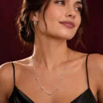 Mujer luciendo Collar Largo de Plata 925 Mujer con detalles ovalados, vestido negro y fondo burdeos de la colección ICONIC.